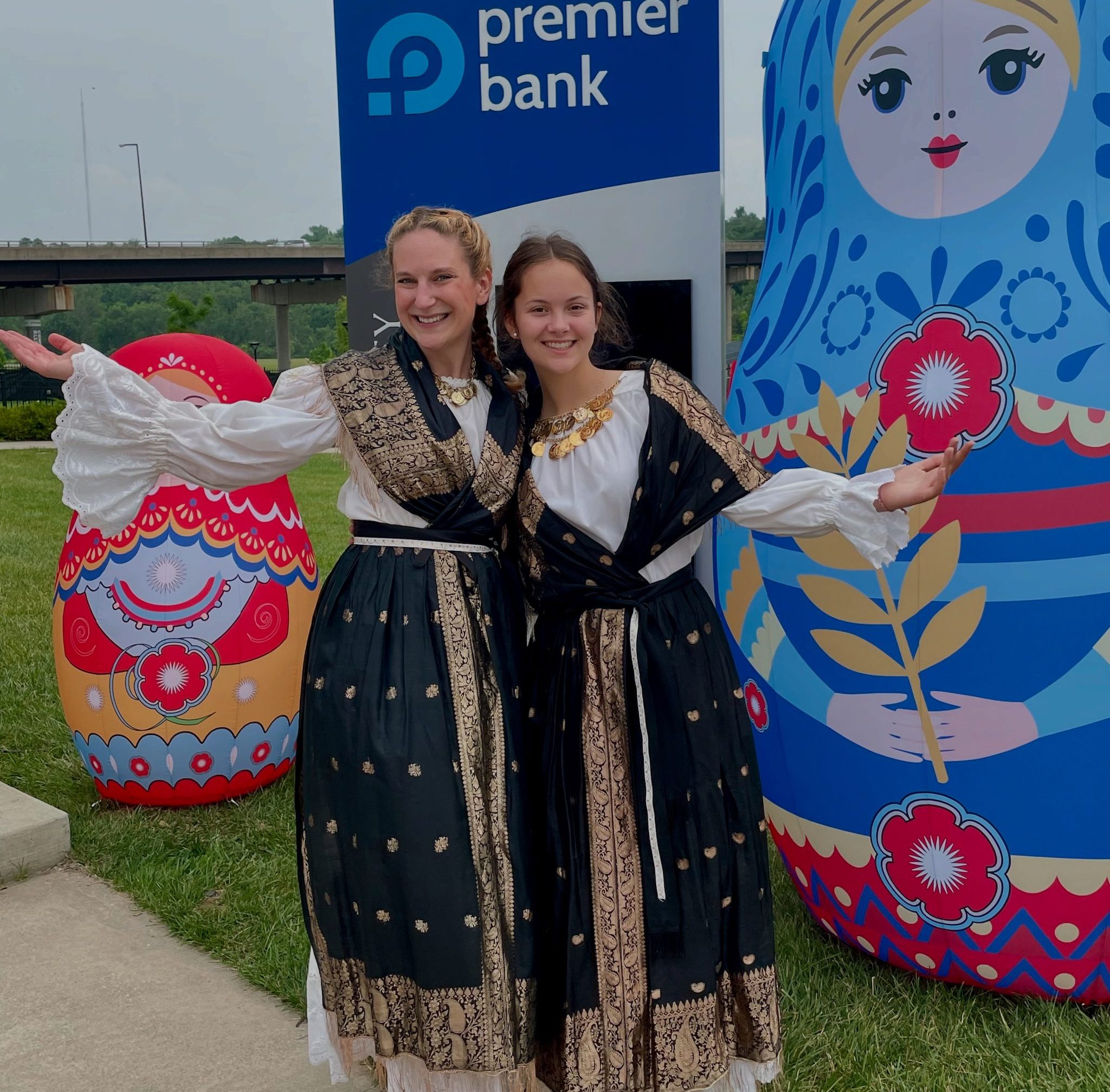 Two people in traditional Slavic clothing in front of traditional dolls